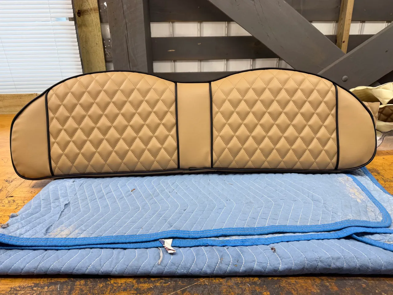 Tan diamond-quilted full-width bench back cushion with black piping on workshop bench